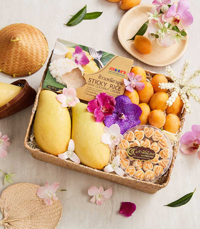 Woven gift basket with Thai mangoes, tropical fruits, coconut sticky rice, heart-shaped cookies, and fresh orchids