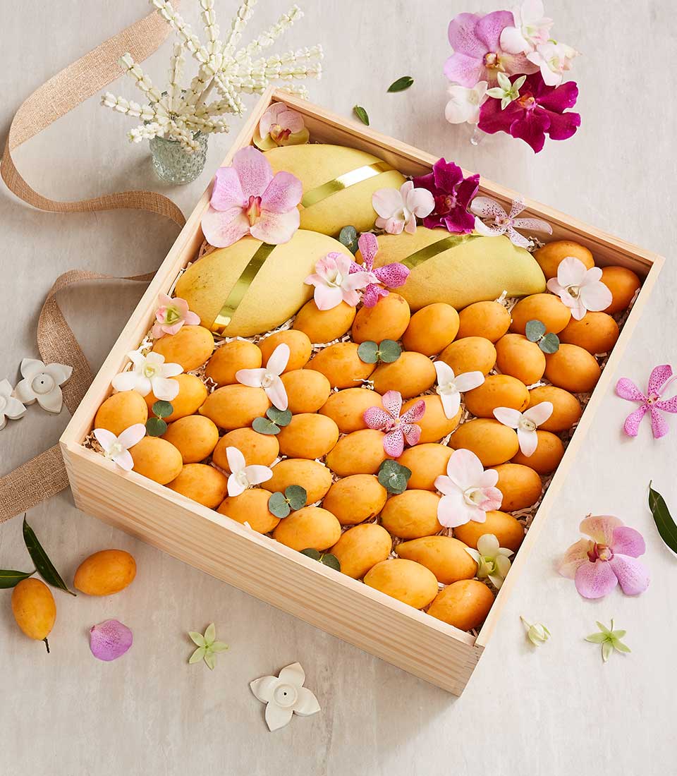 Golden mangoes and Marian plums in artisan wooden box with orchids and tropical fruit arrangement