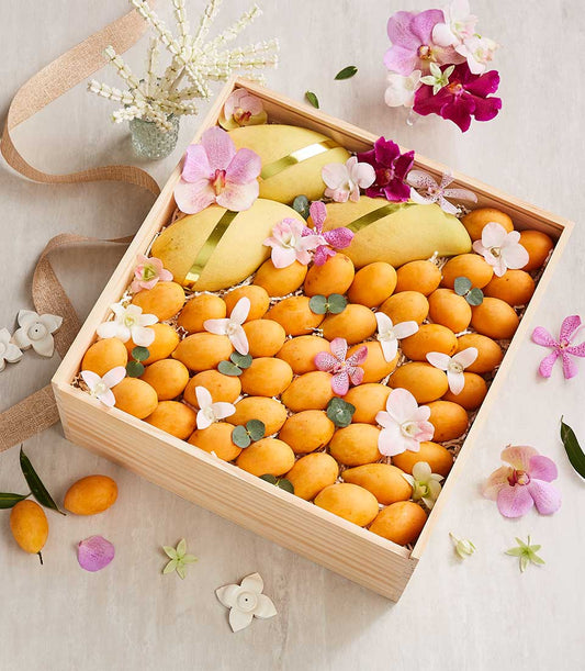 Golden mangoes and Marian plums in artisan wooden box with orchids and tropical fruit arrangement