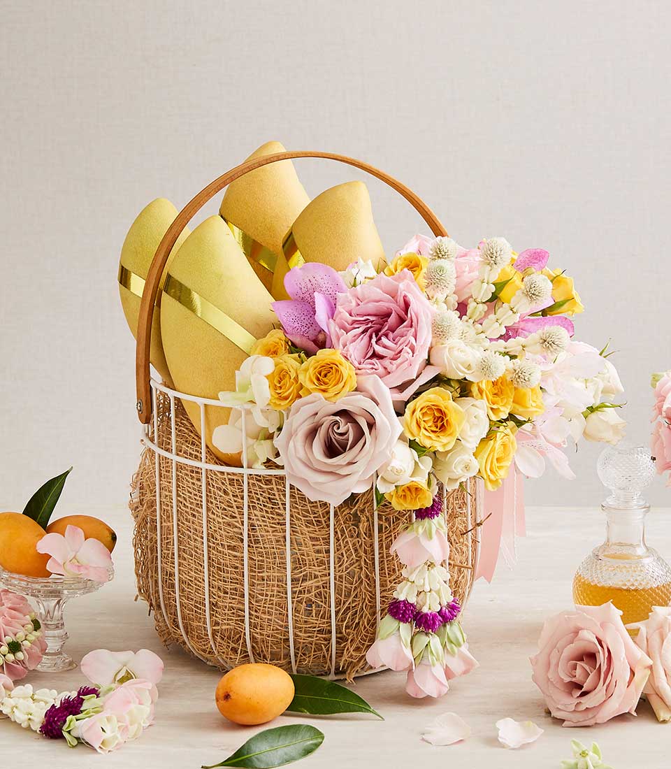 Songkran gift basket with golden mangoes, pink garden roses, orchids, and Thai floral garlands in white wire basket