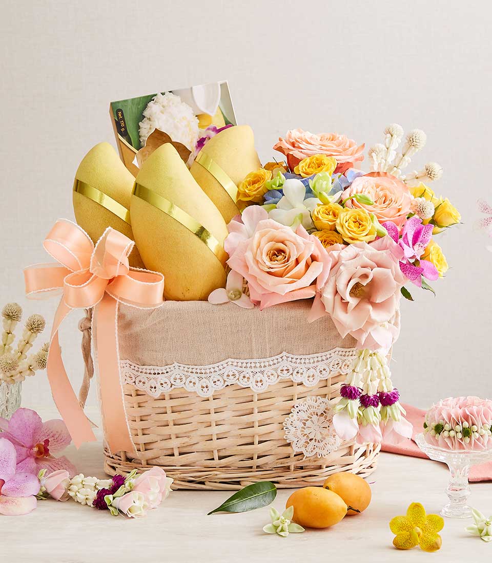 Wicker gift basket with golden mangoes, pink and peach roses, and traditional Thai garland for Songkran celebration