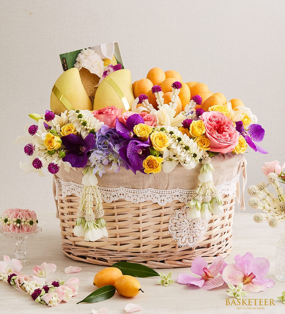 Woven wicker fruit gift basket with yellow mangoes, roses, orchids, hydrangeas, and Thai floral garlands for Songkran