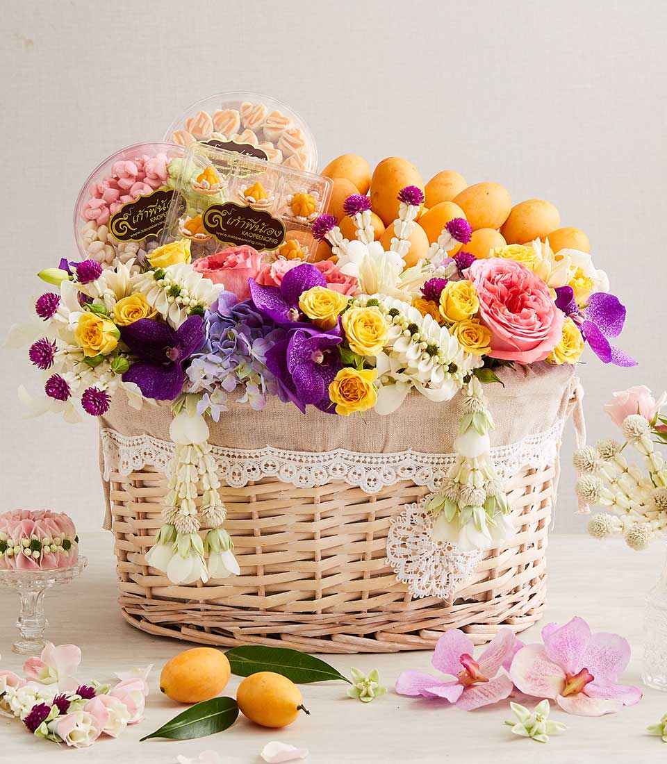 Woven wicker hamper overflowing with pink and yellow roses, purple orchids, fresh mangoes, and Thai sweets for Songkran
