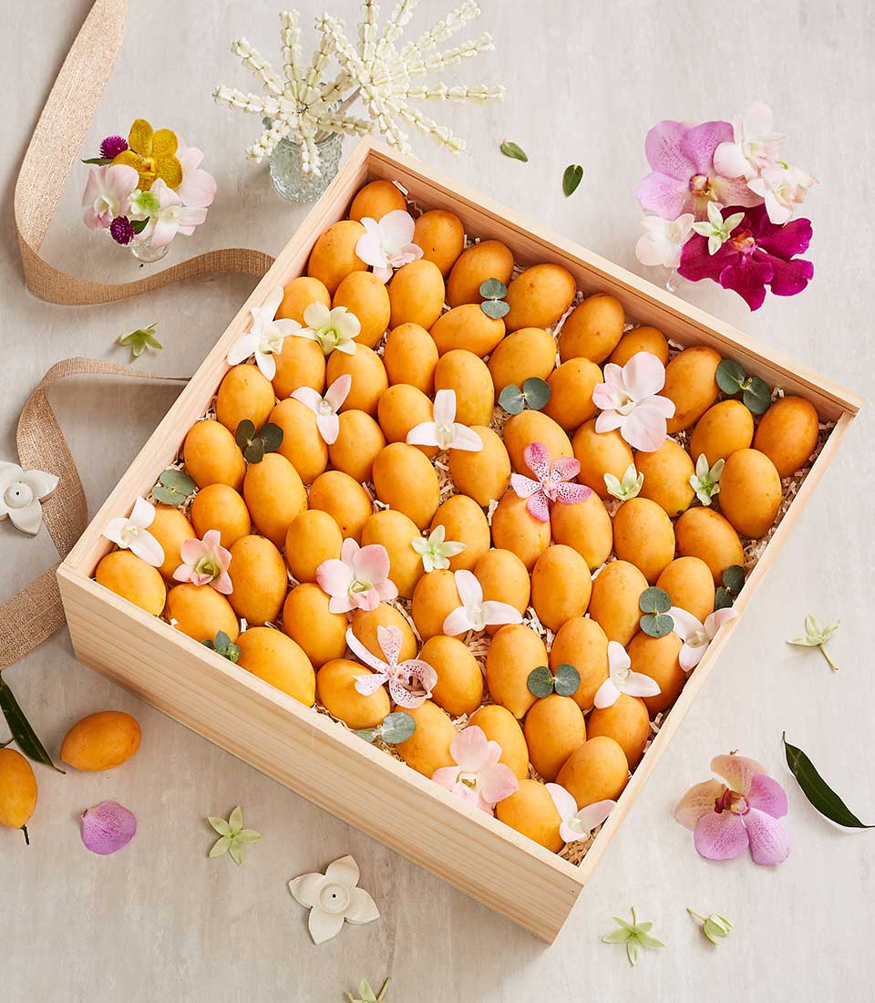 Wooden gift box of golden marian plums with orchid flowers and greenery