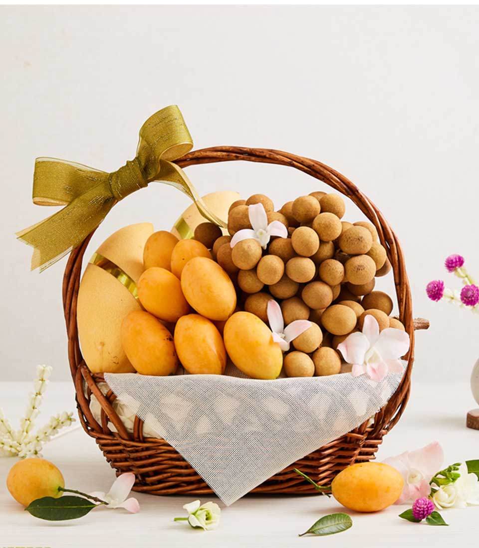 Woven wicker basket filled with fresh Thai mangoes, plums, longans and orchids, tied with golden-green ribbon