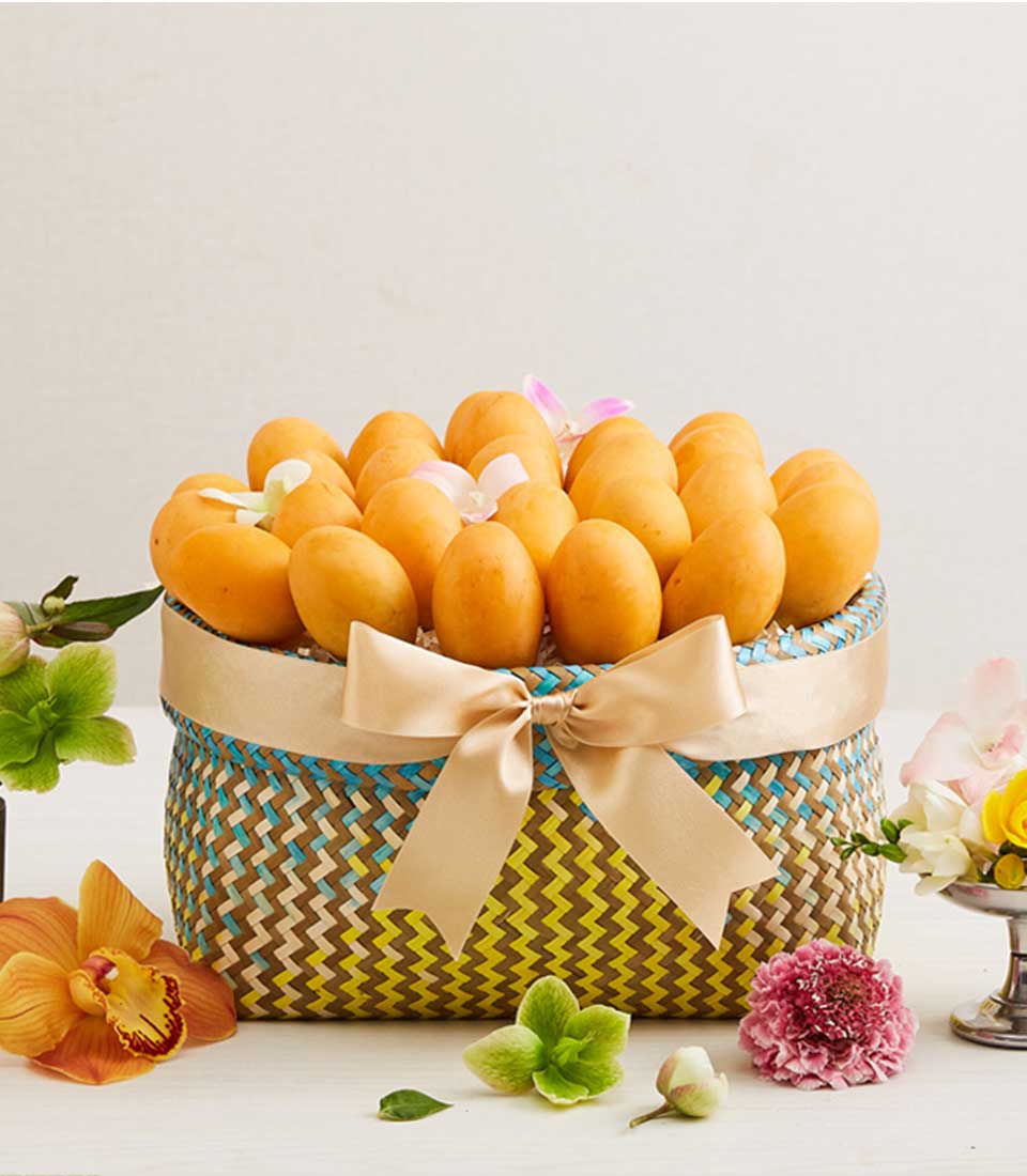 Woven basket of ripe golden mangoes with white and pink orchids and gold satin bow