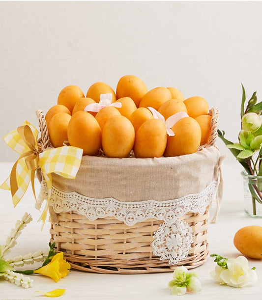 Rustic wicker basket filled with ripe yellow-orange mangoes, lined with beige linen and white lace trim, tied with gingham