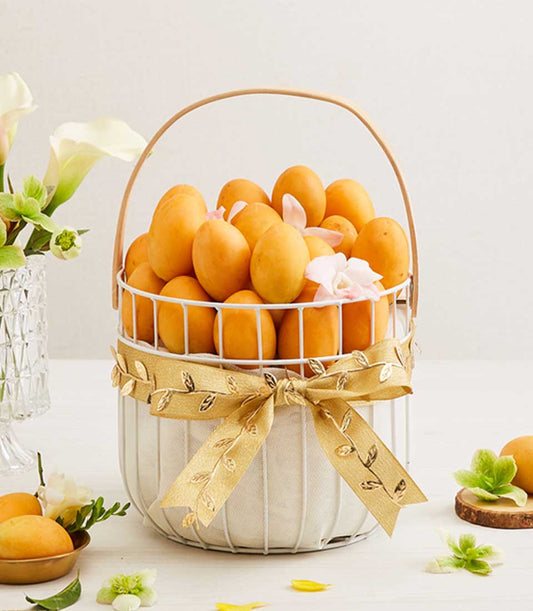 Ripe apricots in white wire basket with gold leaf ribbon, white orchids, calla lilies, and scattered petals
