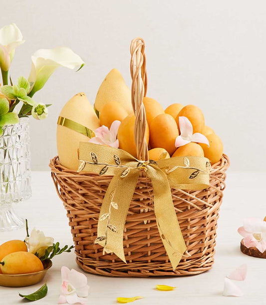 Golden wicker fruit basket filled with ripe yellow and orange mangoes, pink orchids, and golden ribbon bow
