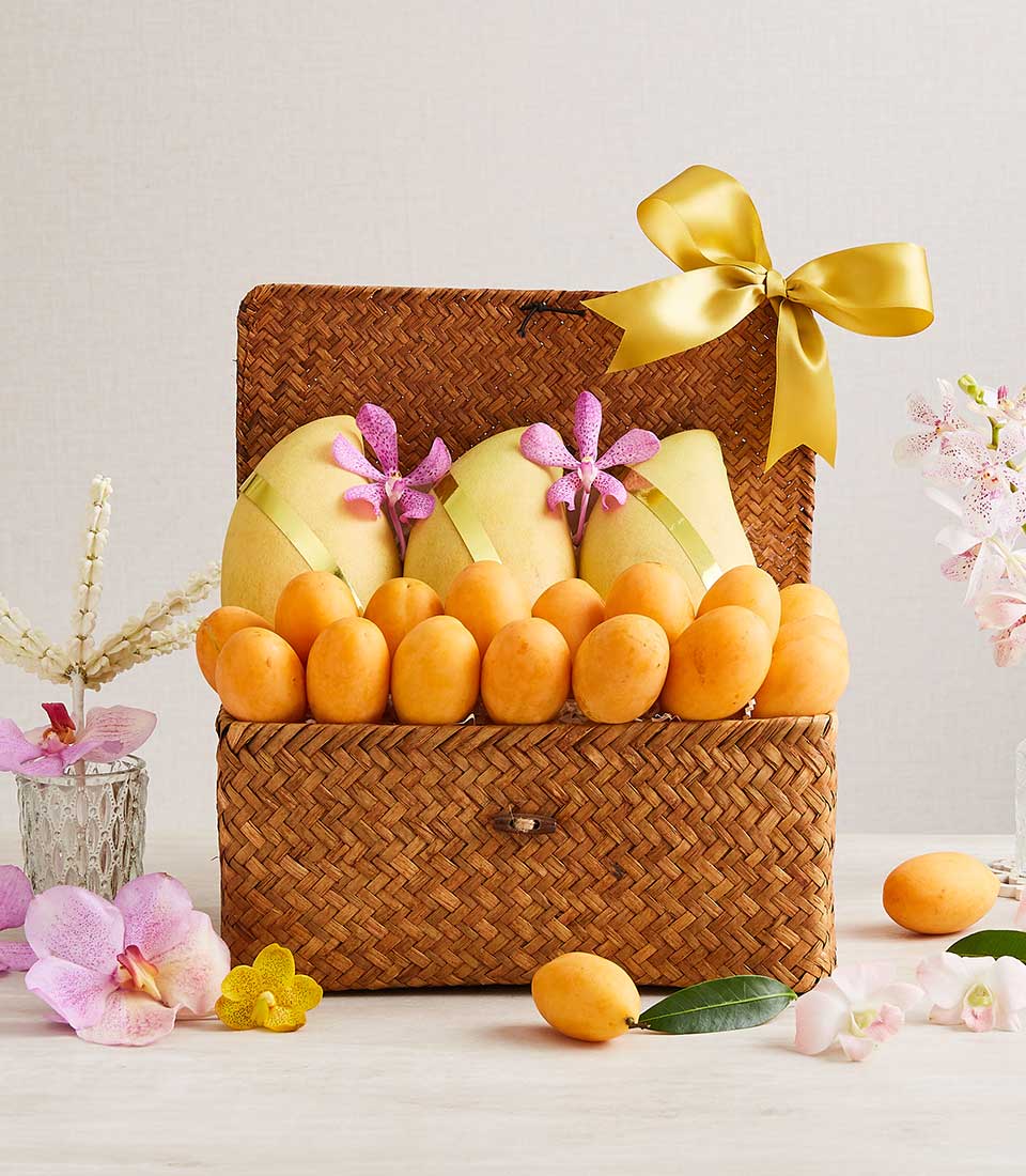 Woven gift basket filled with pale yellow mangoes, purple orchids, and orange Marian plums with gold ribbon