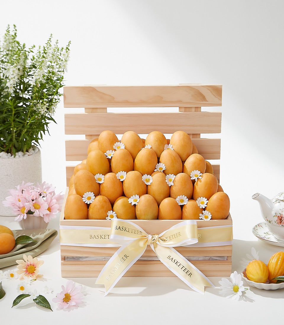 Wooden crate of golden tropical fruits with white daisy accents, tied with yellow Basketeer ribbon