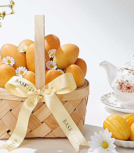 Woven basket of golden apricots with fresh daisies, champagne ribbon, and porcelain tea set
