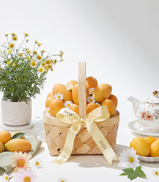 Woven gift basket filled with ripe golden mangoes and white daisies, tied with Basketeer satin ribbon