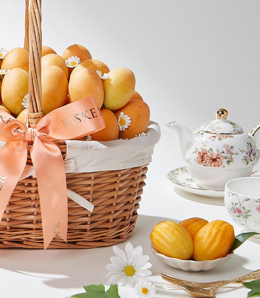 Wicker basket of Thai golden mangoes with white daisies, peach ribbon, and delicate porcelain teapot set