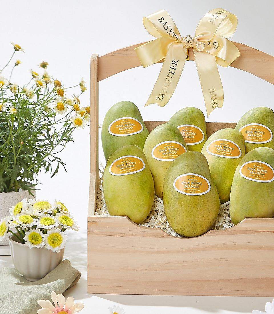Wooden gift basket with nine fresh yellow mangoes, light gold ribbon bow, and summer flowers
