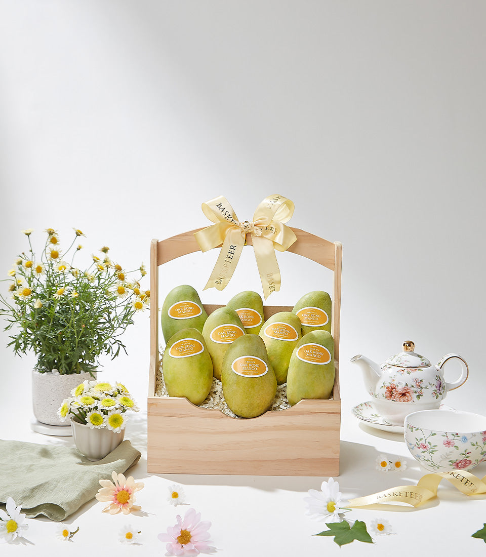 Wooden gift basket with nine fresh green mangoes, gold ribbon bow, and Basketeer branding for premium tropical fruit gifting