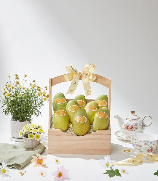 Wooden gift basket with nine fresh green mangoes, gold ribbon bow, and Basketeer branding for premium tropical fruit gifting
