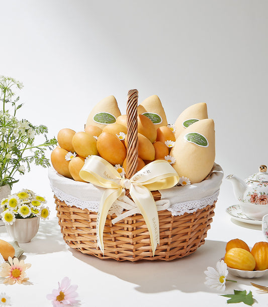 Woven wicker basket filled with golden Nam Dok Mai mangoes, white lace lining, cream ribbon, and fresh daisies
