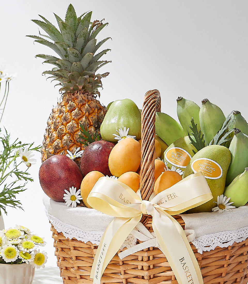 Woven wicker fruit basket with tropical pineapple, mango, pears, passion fruit, and fresh flowers with yellow satin ribbon