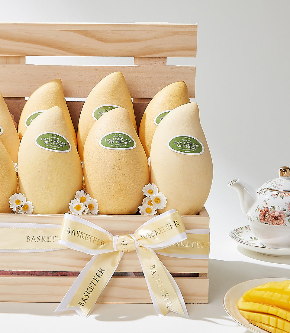 Premium Nam Dok Mai mangoes in golden wood crate with cream ribbon, fresh flowers, and teapot