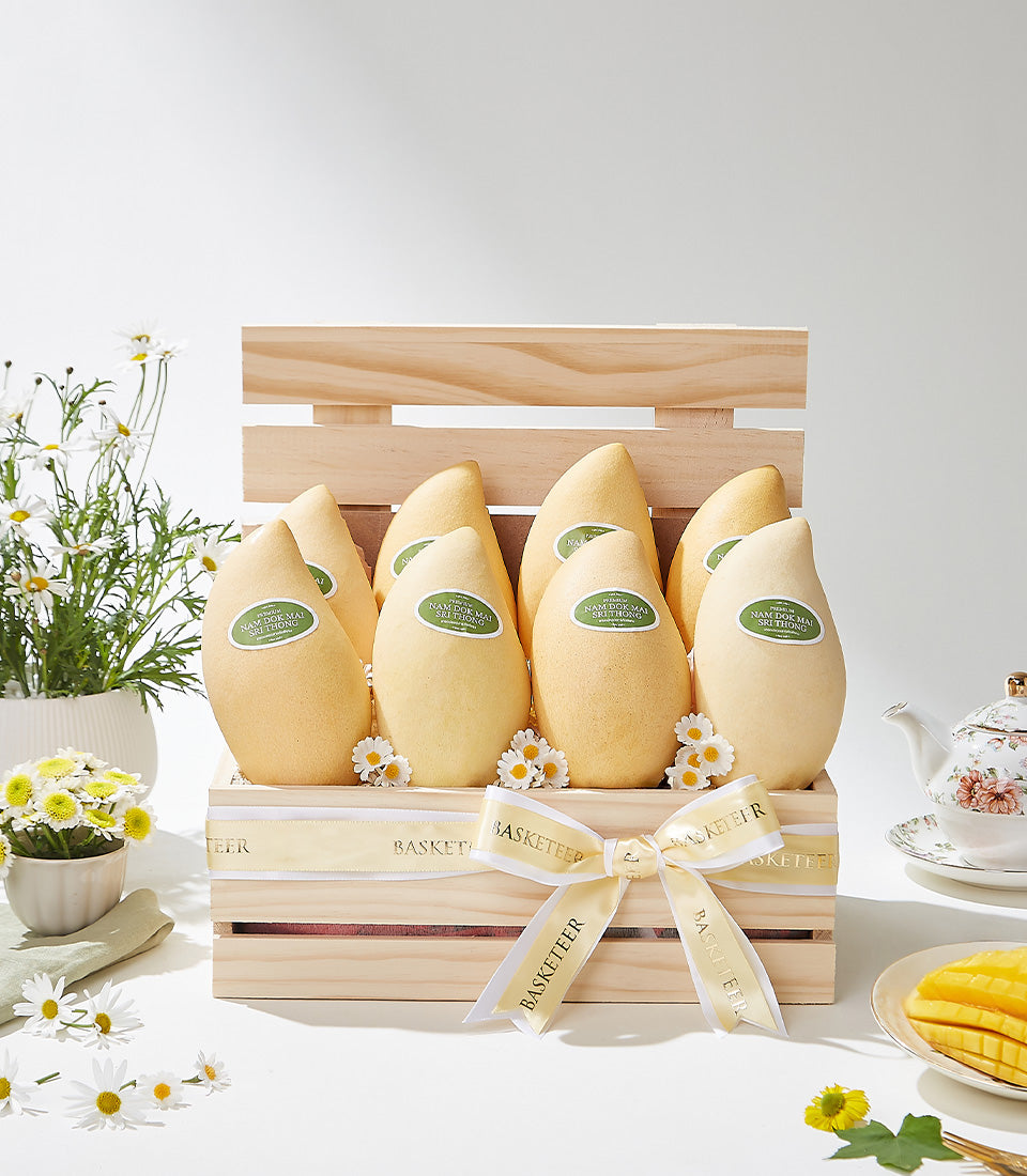 Golden mango gift crate with cream ribbon, white daisies, and ceramic accessories for luxury fruit gifting