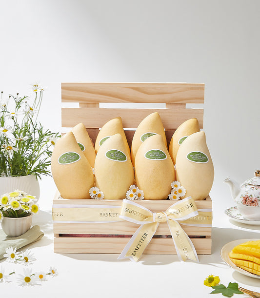 Golden mango gift crate with cream ribbon, white daisies, and ceramic accessories for luxury fruit gifting