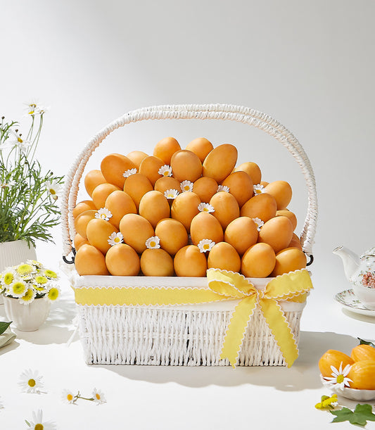 Luxe white wicker basket brimming with golden Thai tropical fruits, yellow ribbon bow, fresh daisy accents