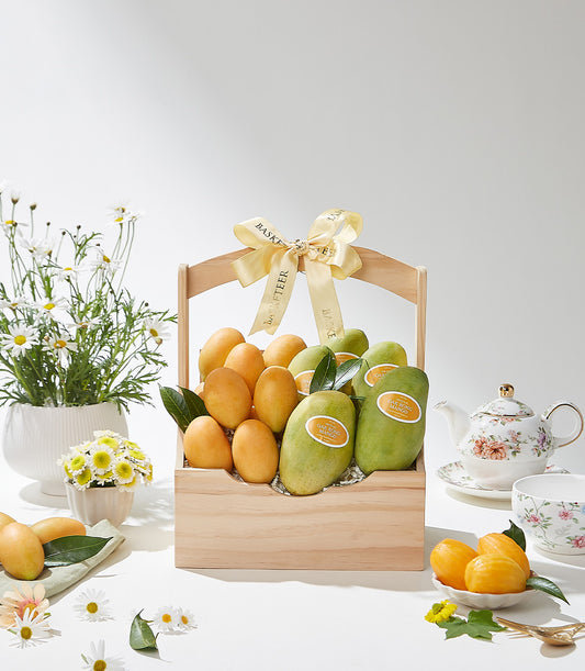Wooden gift basket filled with ripe mangoes and green orchids, tied with gold ribbon, surrounded by fresh white daisies and