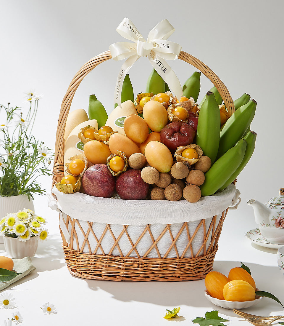 Wicker gift basket filled with fresh Thai tropical fruits including mangoes, passion fruits, longans, and berries, tied with
