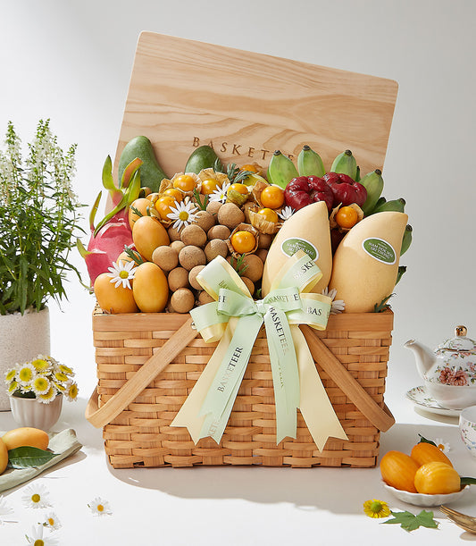 Woven wicker basket overflowing with fresh Thai tropical fruits, mangoes, dragon fruit, and longans, tied with green ribbon