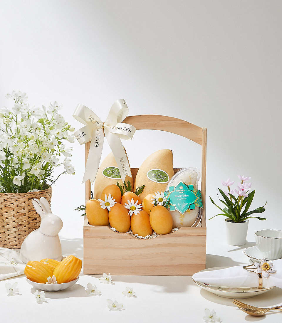 Wooden gift basket with fresh mangoes, sticky rice, and white daisy flowers for tropical summer gifting