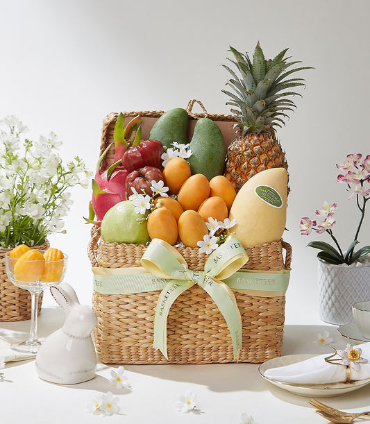 Woven fruit basket filled with tropical pineapple, mangoes, dragon fruit and guava with green ribbon bow