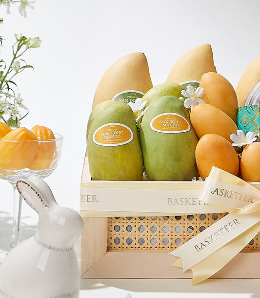 Tropical fruit gift basket with fresh yellow mangoes and green Oaks, white flowers, and cream ribbon bow