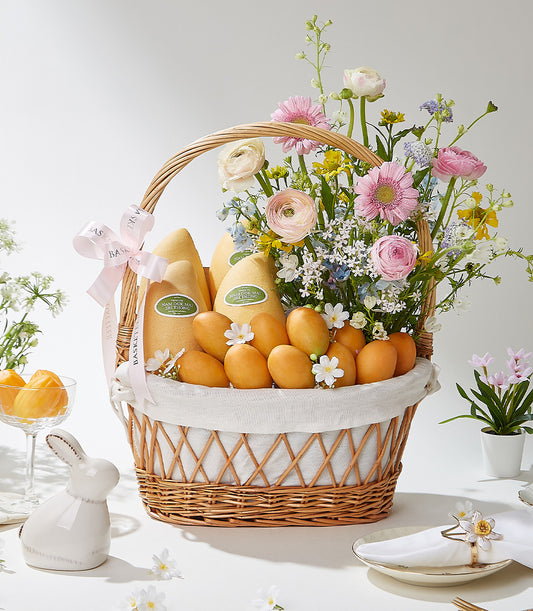 Vibrant Thai tropical fruit basket with fresh mangoes, pink gerberas, ranunculus, and wildflowers in wicker