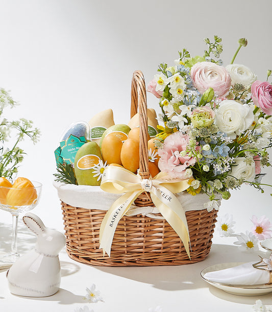 Woven wicker gift basket with fresh Thai mangoes, sticky rice, and spring flower bouquet tied with cream ribbon