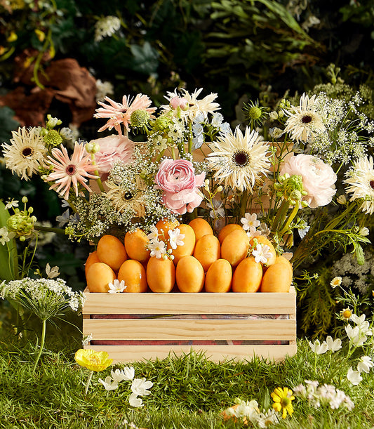 Golden Harvest tropical fruit crate with pink and white gerberas, roses, and baby's breath arrangement