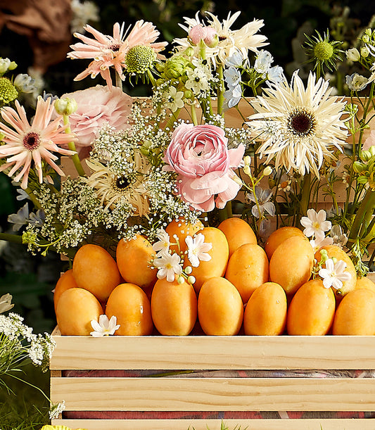 Wooden crate of golden Thai tropical fruits with pink and white gerbera daisies, ranunculus, and baby's breath