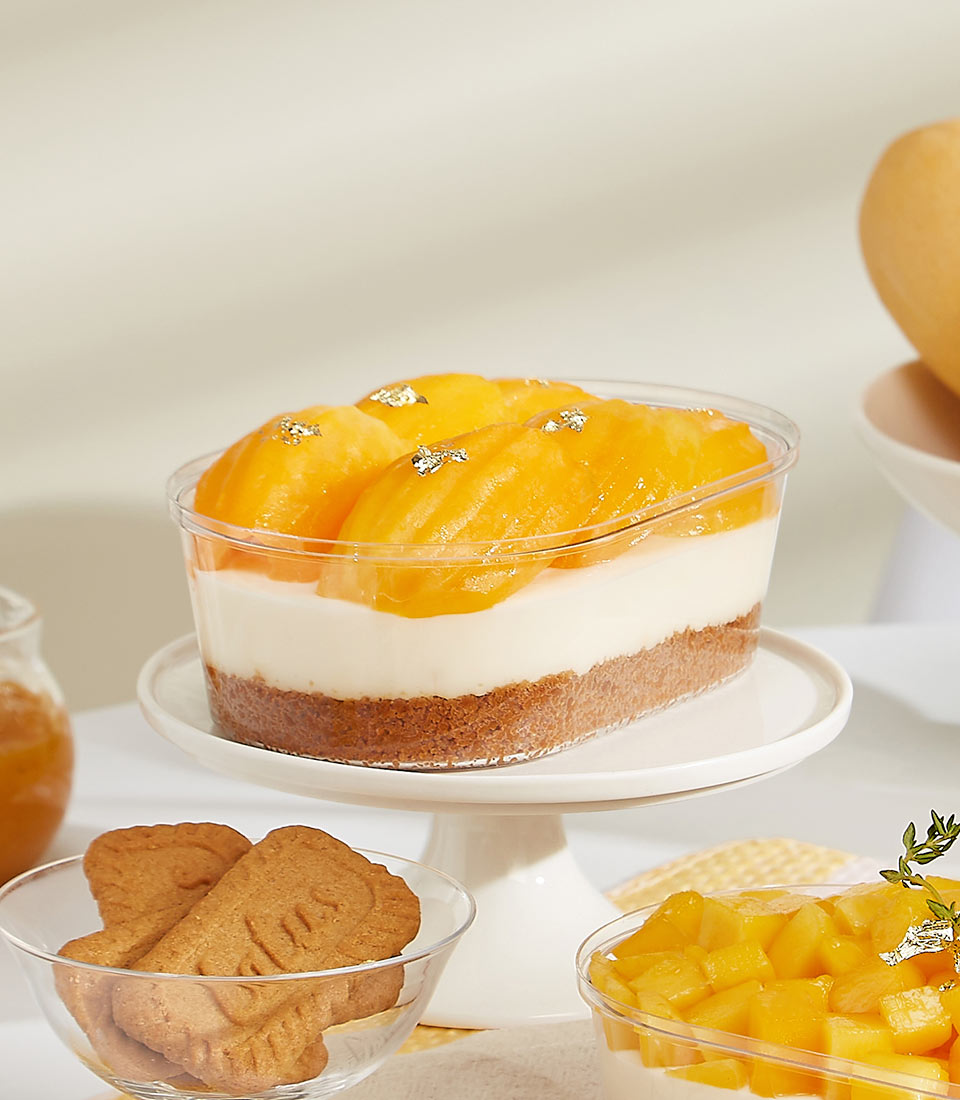 Layered Biscoff cheesecake with fresh mango and gold leaf on white cake stand, served with Biscoff cookies