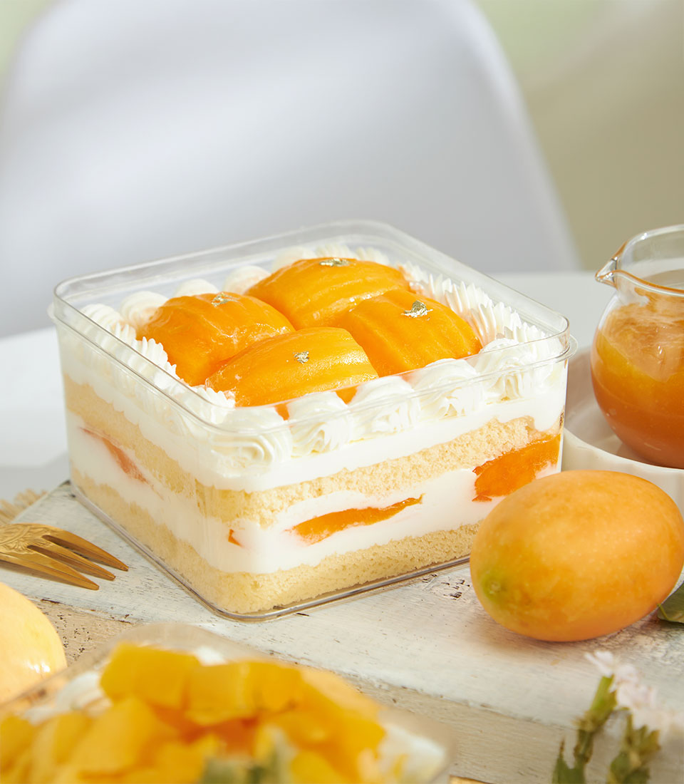 Layered mango trifle cake with fresh cream, sponge, and tropical fruit in clear container