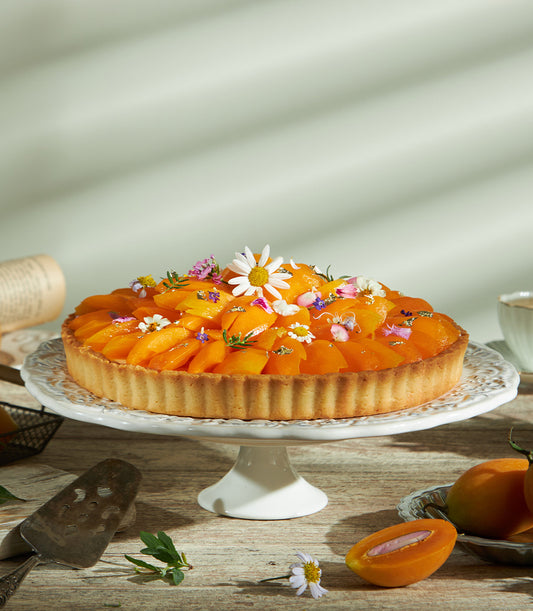 Golden Mayongchid mango tart with edible flowers and gold leaf on ceramic stand