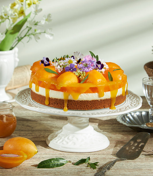 Mango cheesecake with Biscoff crust, fresh mango glaze, and edible flowers on ceramic cake stand