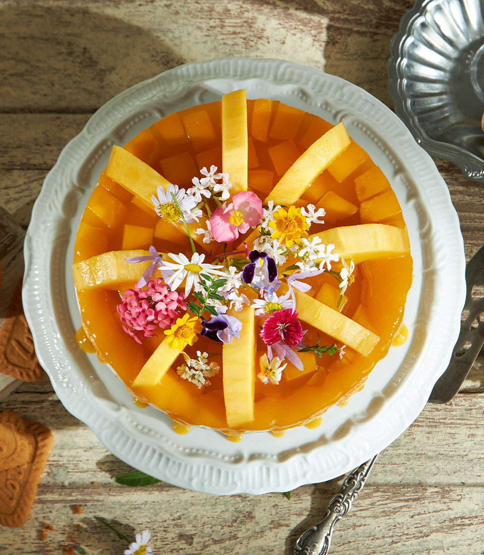 Sun-kissed mango cheesecake with fresh edible flowers and melon, artisan celebration cake on scalloped ceramic plate