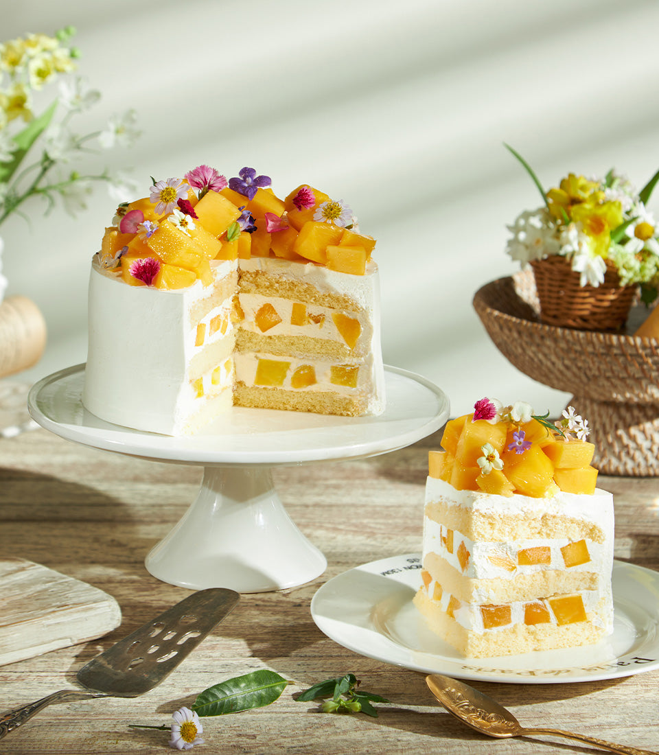 Super soft fresh cream mango cake with white frosting, layered mango pieces, and edible flowers on ceramic stand