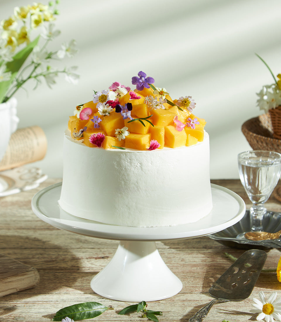 Super soft fresh cream mango cake with diced mango and edible flowers on white ceramic stand