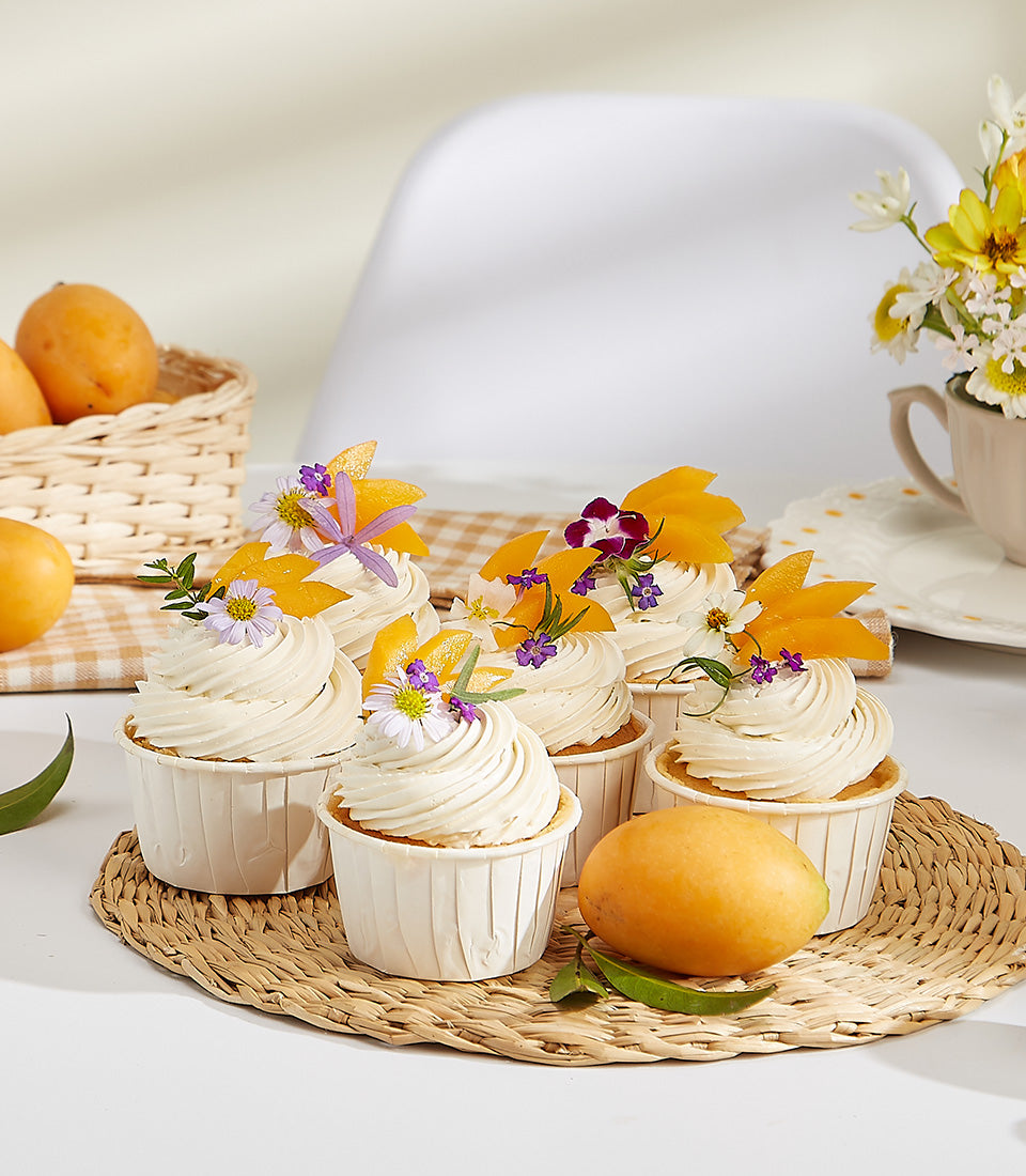 Citrus Glow Mayongchid cupcakes with white frosting, candied citrus, and edible flowers on woven mat