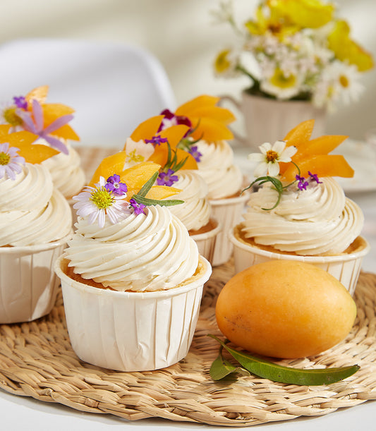 Citrus Glow Mayongchid cupcakes with mango slices, purple flowers, and fresh tropical fruit garnish