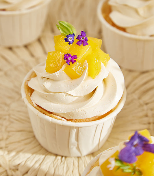 Mango passion summer cupcake with white frosting, diced tropical fruit, and edible flowers