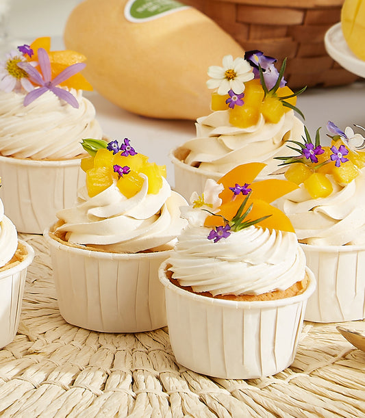 Mango cupcakes with fresh fruit, white frosting, and purple flowers on woven mat