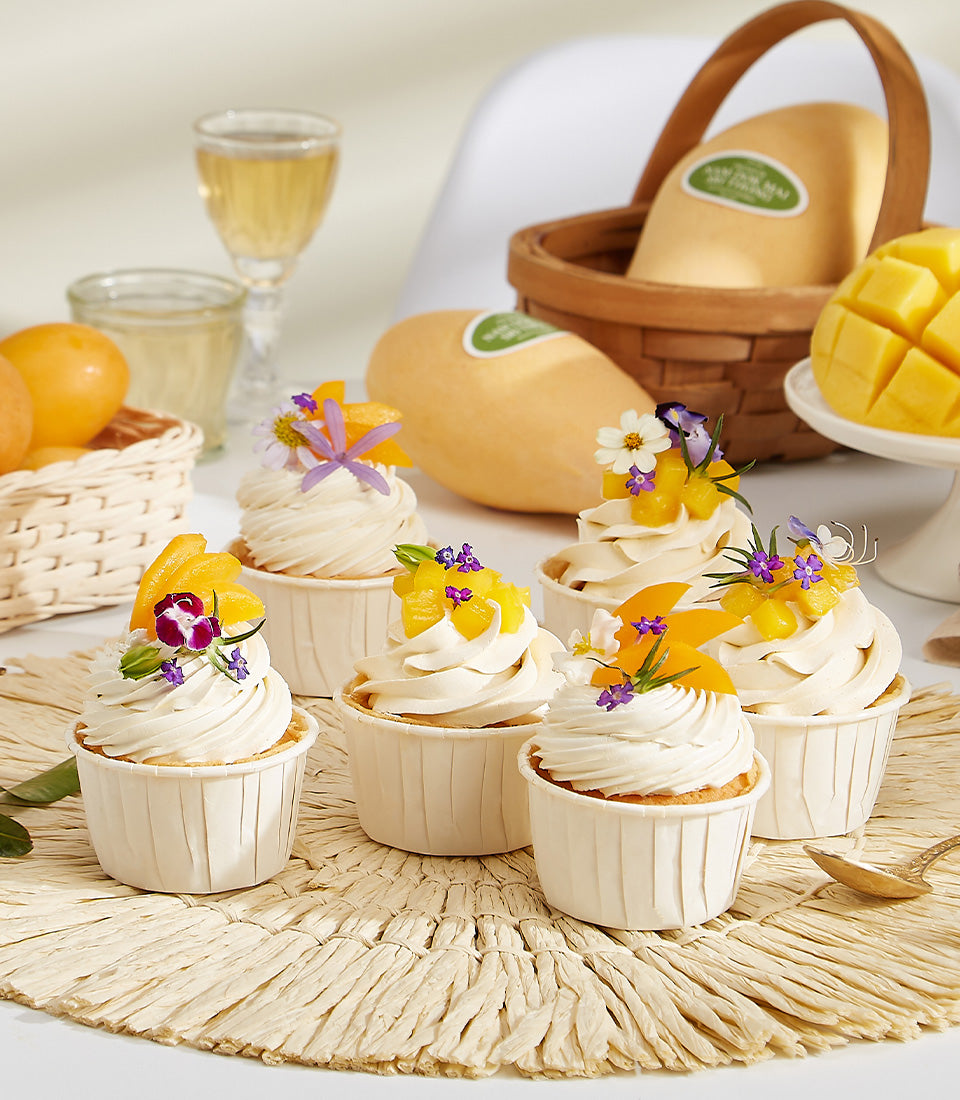 Fresh mango cupcakes with yellow frosting and edible flowers, artisan summer bakery gift