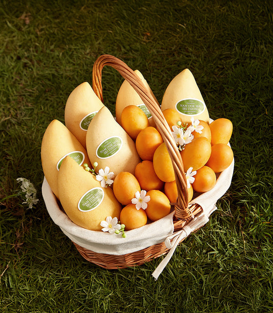 Woven wicker basket filled with premium Thai mangoes and mayongchid fruits, white ribbon bow, fresh floral accents